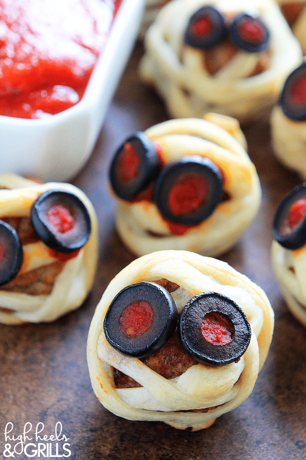 These Meatball Mummies are a fun, easy, and delicious Halloween finger food idea. They are store-bought meatballs, wrapped in crescent down, and topped with marinara and olives.