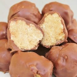 Plate of Chocolate Peanut Butter Balls with one ball cut in half, showing the insides with the rice krispy, peanut butter filling.