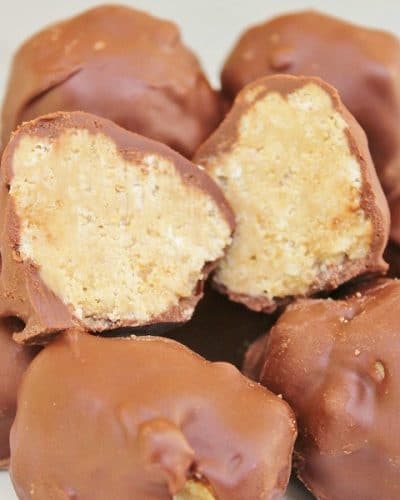 Plate of Chocolate Peanut Butter Balls with one ball cut in half, showing the insides with the rice krispy, peanut butter filling.