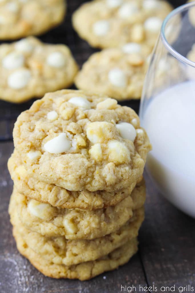 Stack of White Chocolate Chip Macadamia Nut Cookies, paired with a glass of milk and cookies on a cooling rack in the background.