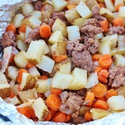 Ground beef, carrots, potatoes, and onions laid out in aluminum foil to make up a tin foil dinner packet.