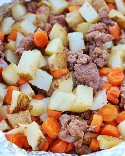 Ground beef, carrots, potatoes, and onions laid out in aluminum foil to make up a tin foil dinner packet.