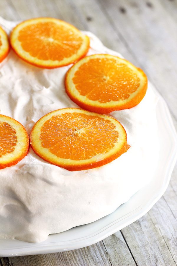 Skinny Orange Creamsicle Cake - a low calorie cake. Whole cake on plate. Whipped topping icing with orange slices on top.