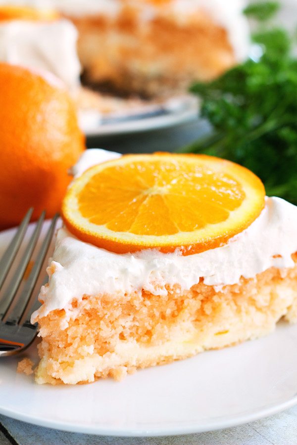 Skinny Orange Creamsicle Cake - a low calorie cake. Single slice of cake on plate, with fork, whole cake in background