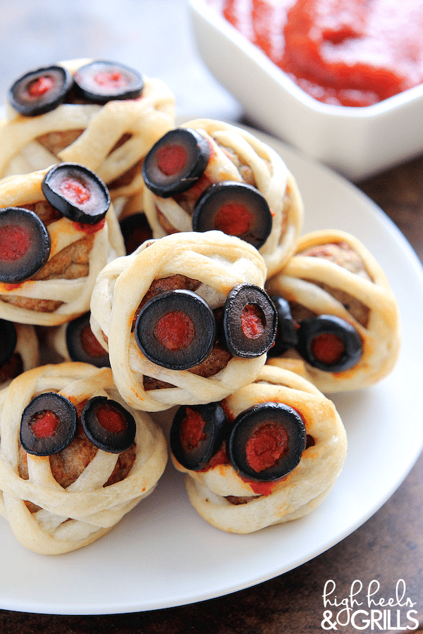 These Meatball Mummies are a fun, easy, and delicious Halloween finger food idea. They are store-bought meatballs, wrapped in crescent down, and topped with marinara and olives.
