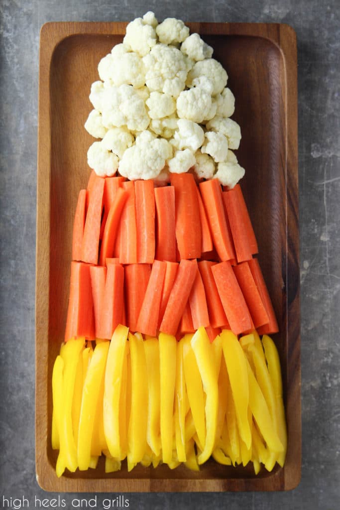 Candy Corn Halloween Veggie Tray with yellow peppers on the bottom, orange carrots in the middle, and white cauliflower on top. Shaped in a triangle to look like candy corn