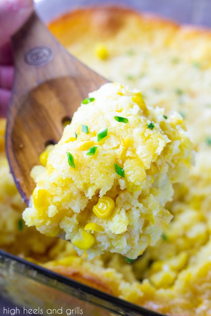Serving spoon holding Easy Corn Casserole with pan of of the casserole in the background.