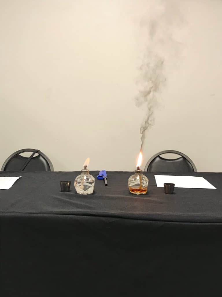 Ethanol versus gasoline burning. The gasoline is giving off a thick, black smoke, while the ethanol is clear.