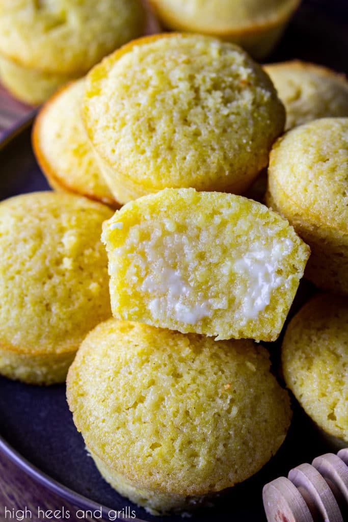 A pile of sweet cornbread muffins with honey drizzled on the tops. The middle one split in half with butter soaking into it.